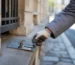 Main gantée plaçant un piège à rats professionnel lors d'une intervention de dératisation près d’un mur en pierre d’immeuble parisien, focus sur la prévention des nuisibles en milieu urbain.