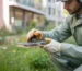 Professionnel en dératisation écologique installant un piège sans poison dans un jardin urbain fleuri, mains gantées manipulant l’outil, plantes vertes et fleurs colorées en arrière-plan, solution de dératisation respectueuse de l’environnement.