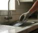 Main gantée installant un piège à rats moderne sous un évier de cuisine propre, illustration professionnelle de dératisation dans un intérieur moderne.